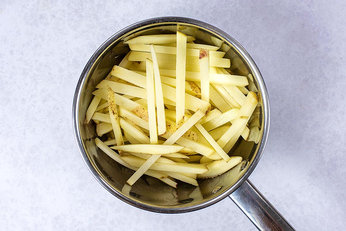 A saucepan full of potatoes cut into fries.