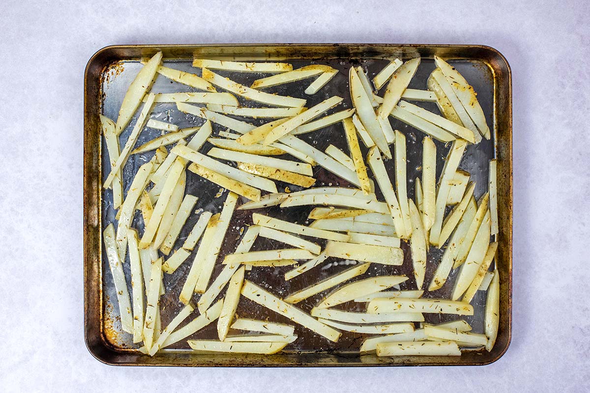 A baking tray covered in parboiled and seasoned fries.