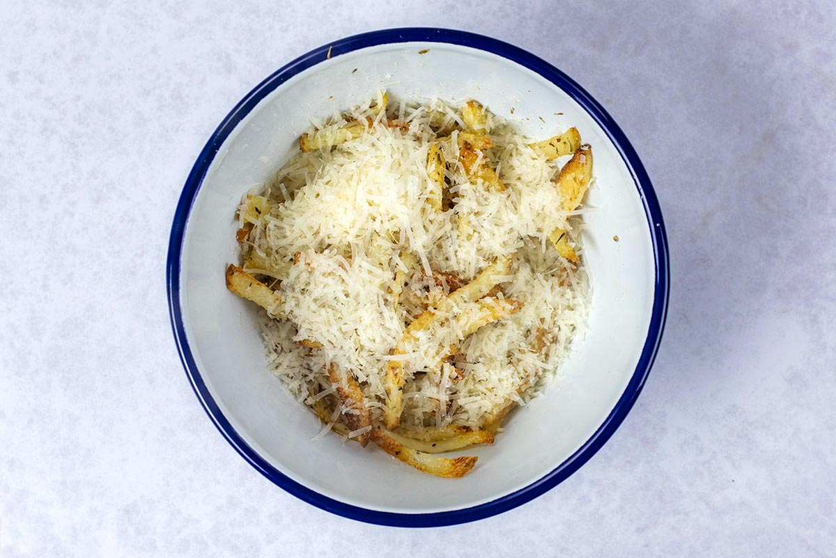 Cooked fries in a bowl covered in grated Parmesan cheese.