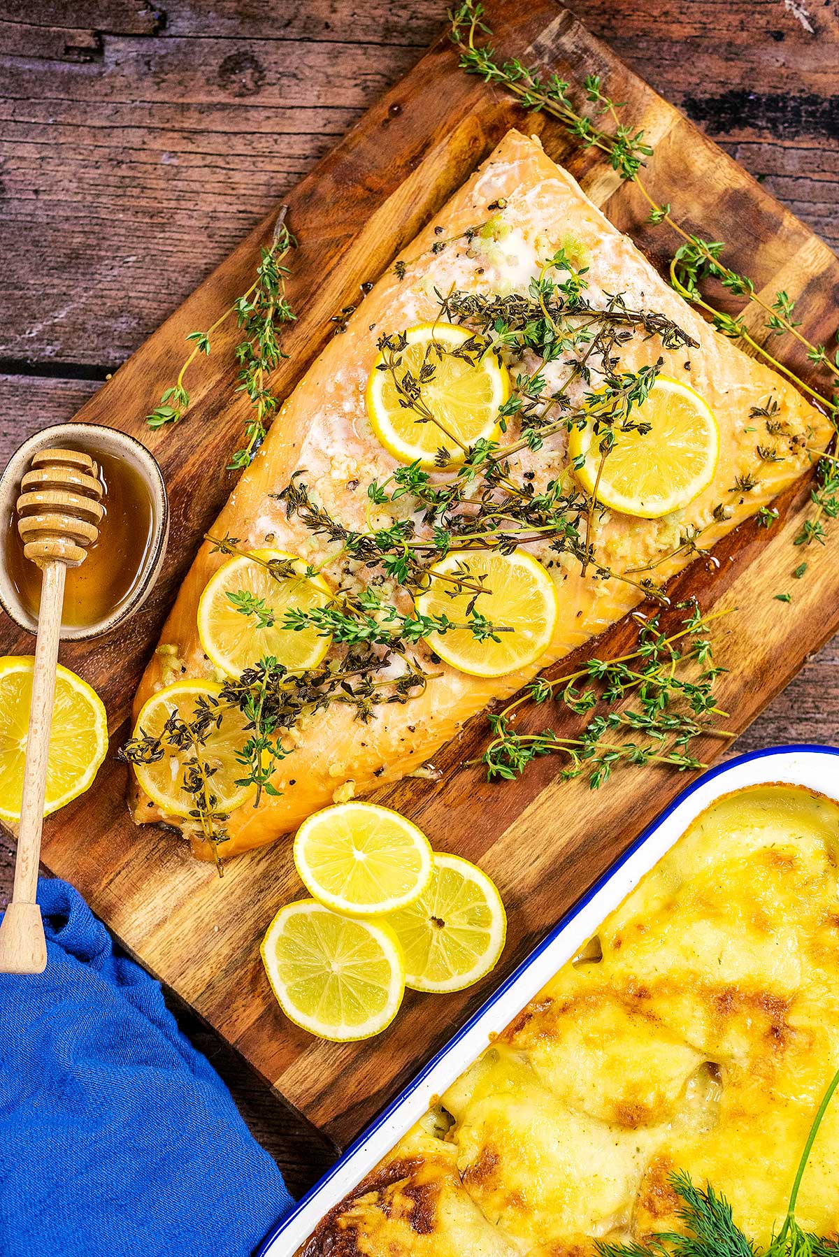 A side of cooked salmon on a wooden serving board topped with slices of lemon and sprigs of thyme.