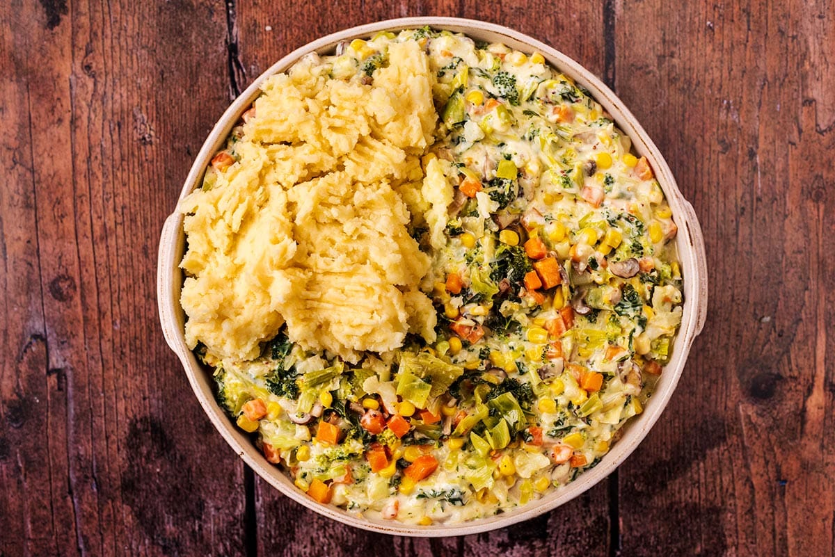 The cheesy vegetables in a large dish with the mashed potato being put over the top.