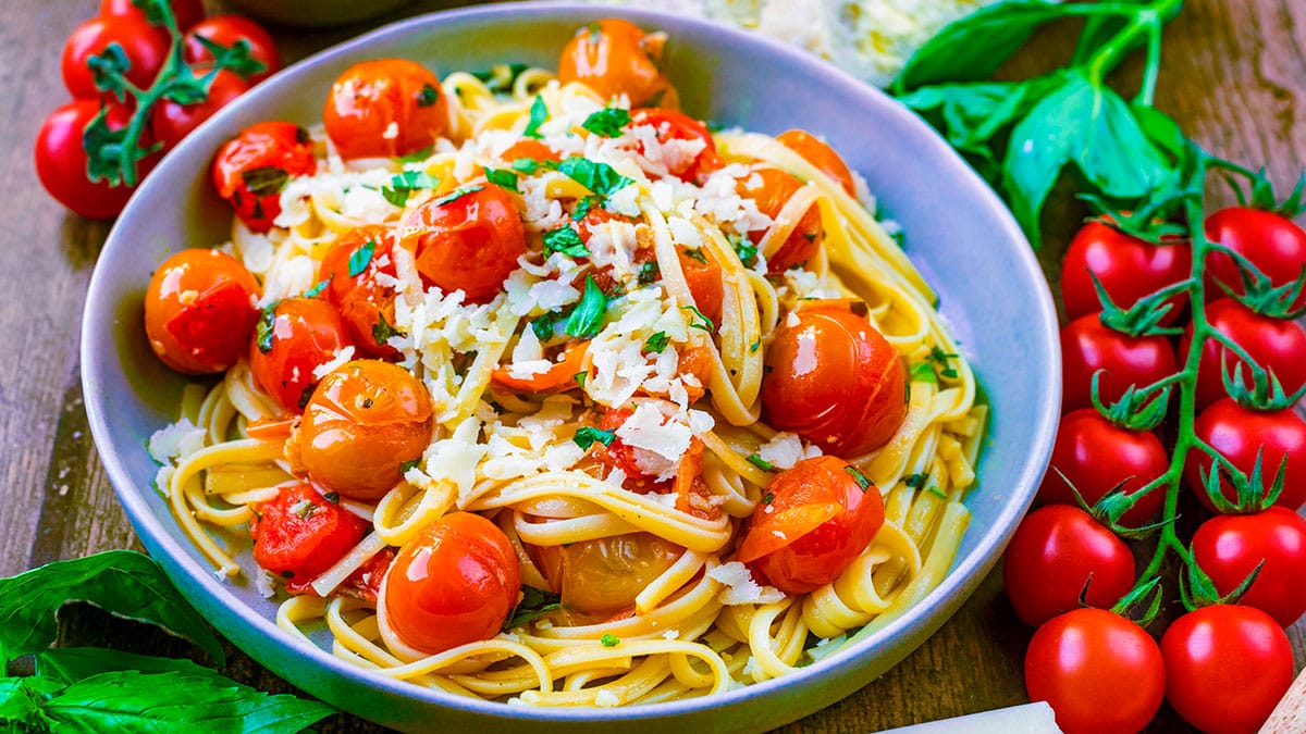 Cherry tomatoes and linguine in a bowl topped with parmesan shavings and chopped basil.