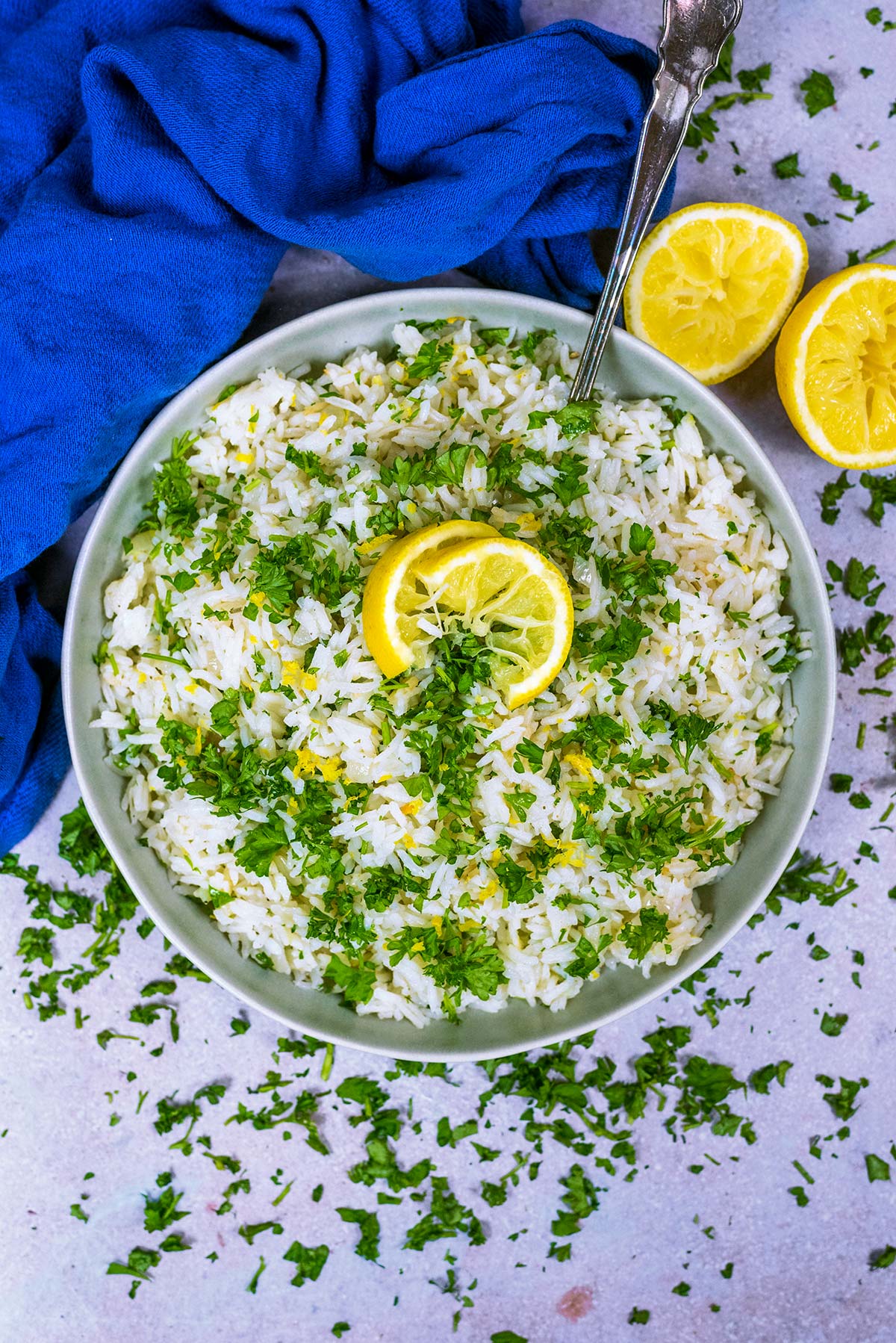 A large bowl of cooked rice, topped with chopped herbs and slices of lemon.