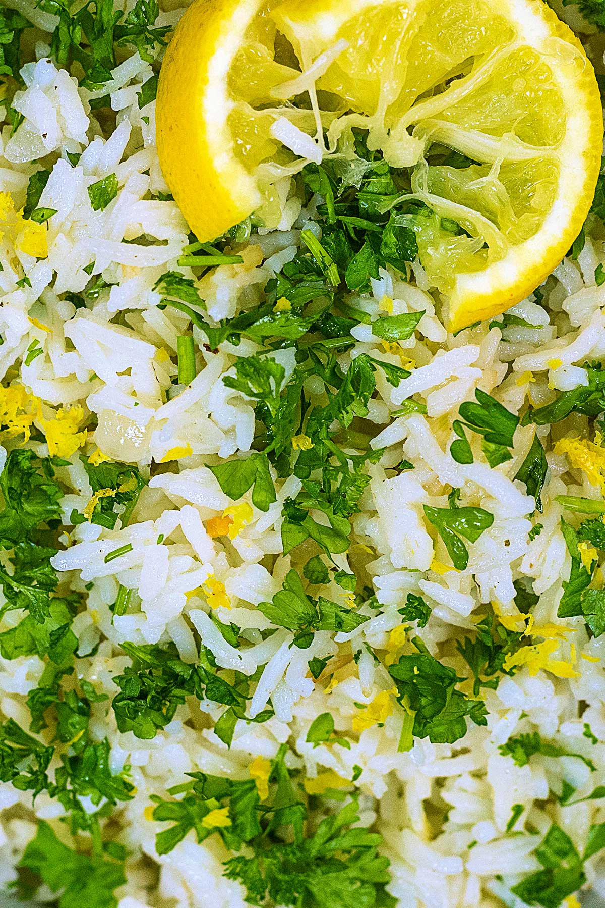 Cooked rice mixed with chopped parsley and lemon zest. A lemon slice is on top.