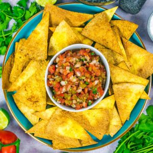 Air fryer tortilla chips on a plate with a bowl of salsa.