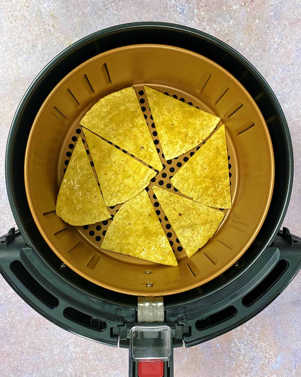 An air fryer basket with tortilla chips laid in a single layer.