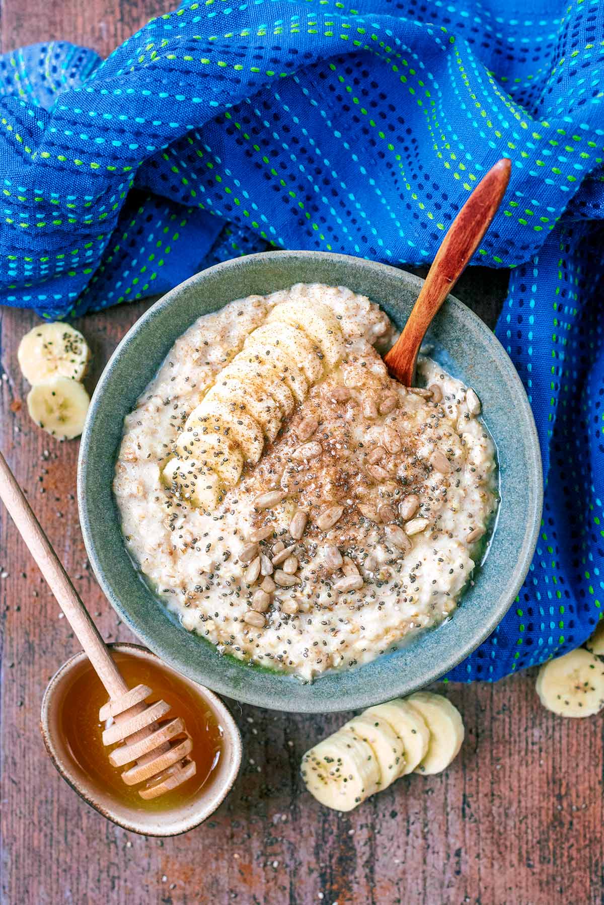 A bowl of porridge topped with banana slices, honey and seeds.