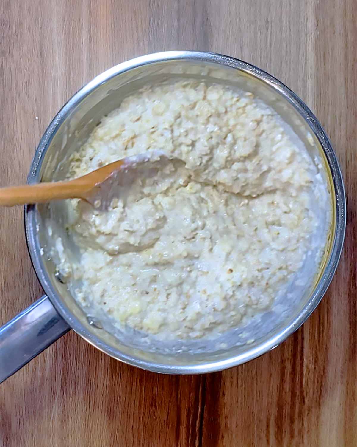 A saucepan of porridge with a wooden spoon mixing it.