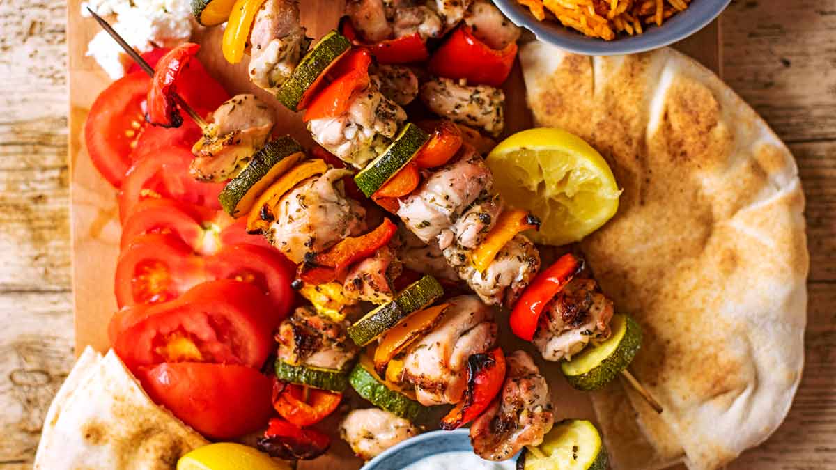 Greek chicken skewers and flatbreads on a wooden board..