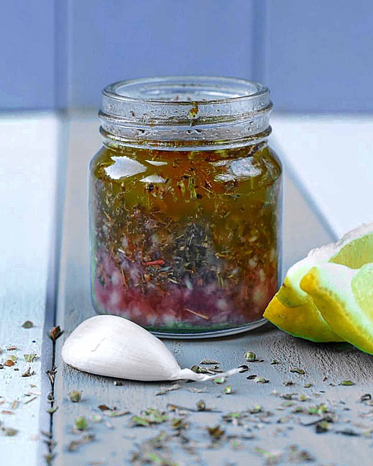A small jar full of oil mixed with chopped herbs.