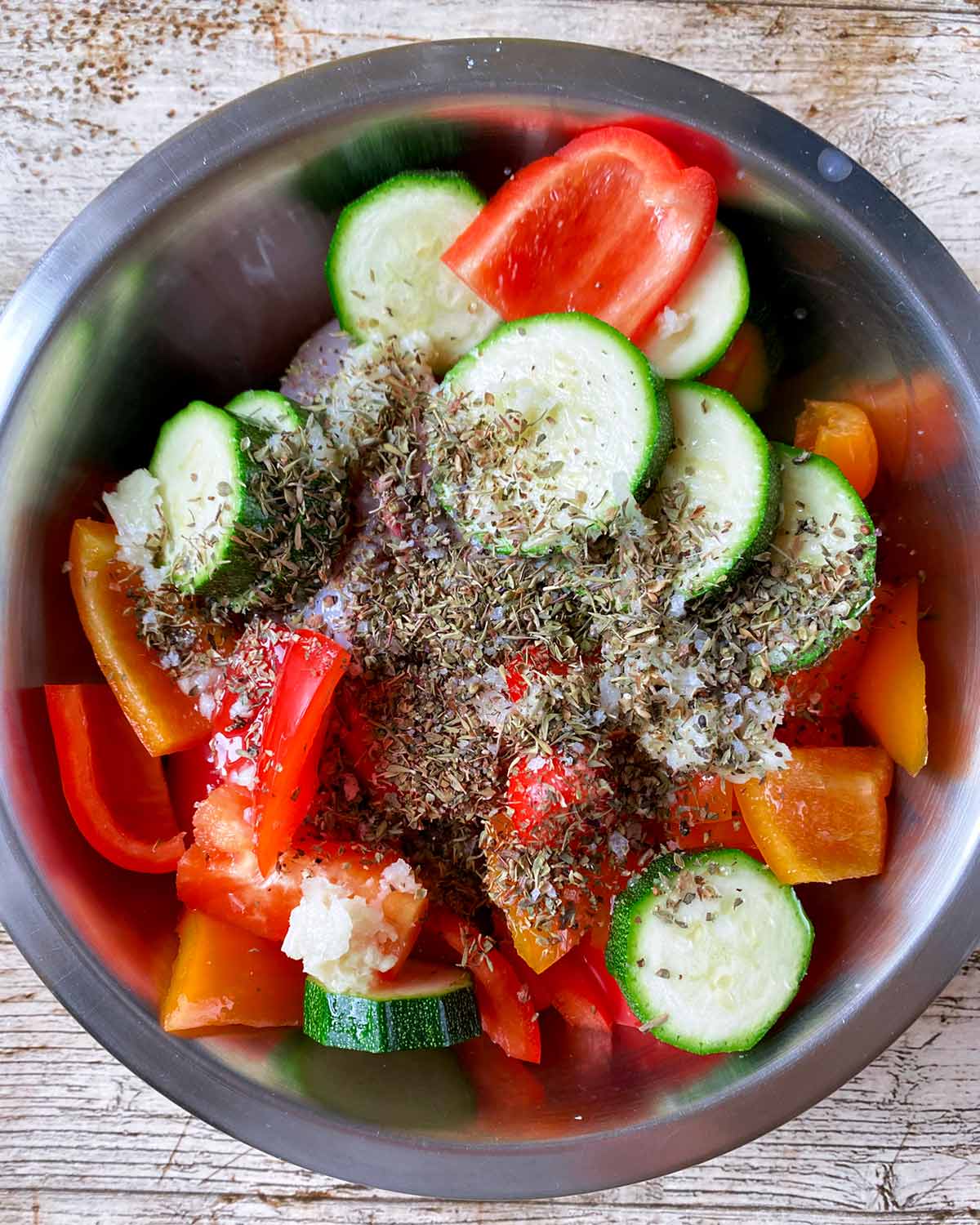 A metal mixing bowl containing chicken and vegetables all covered in a herb marinade.