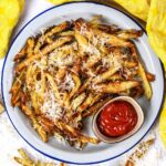 A plate of parmesan truffle fries with a pot of ketchup.