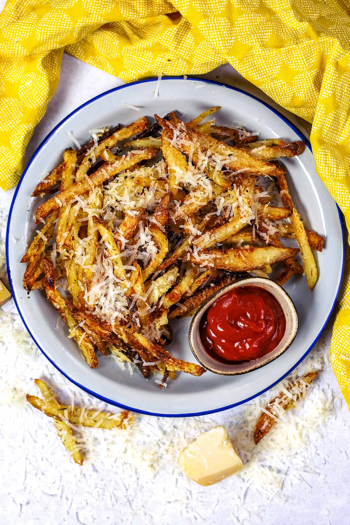 A plate of cheese covered fries with a small pot of ketchup.