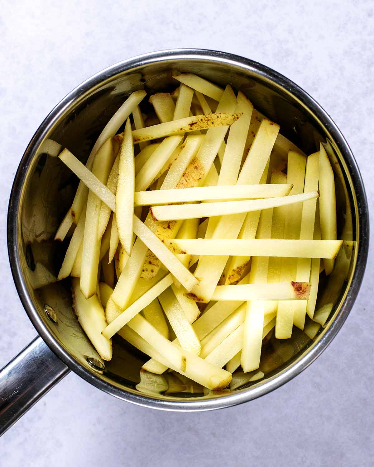 A saucepan full of potatoes cut into fries.