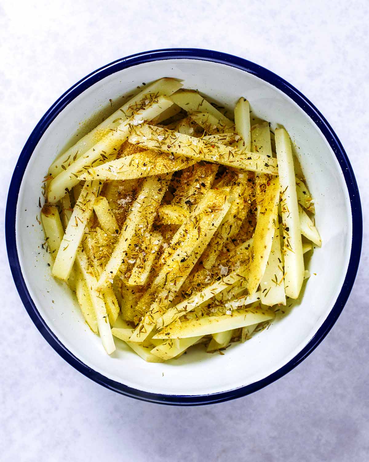 A large mixing bowl with parboiled fries and seasoning.