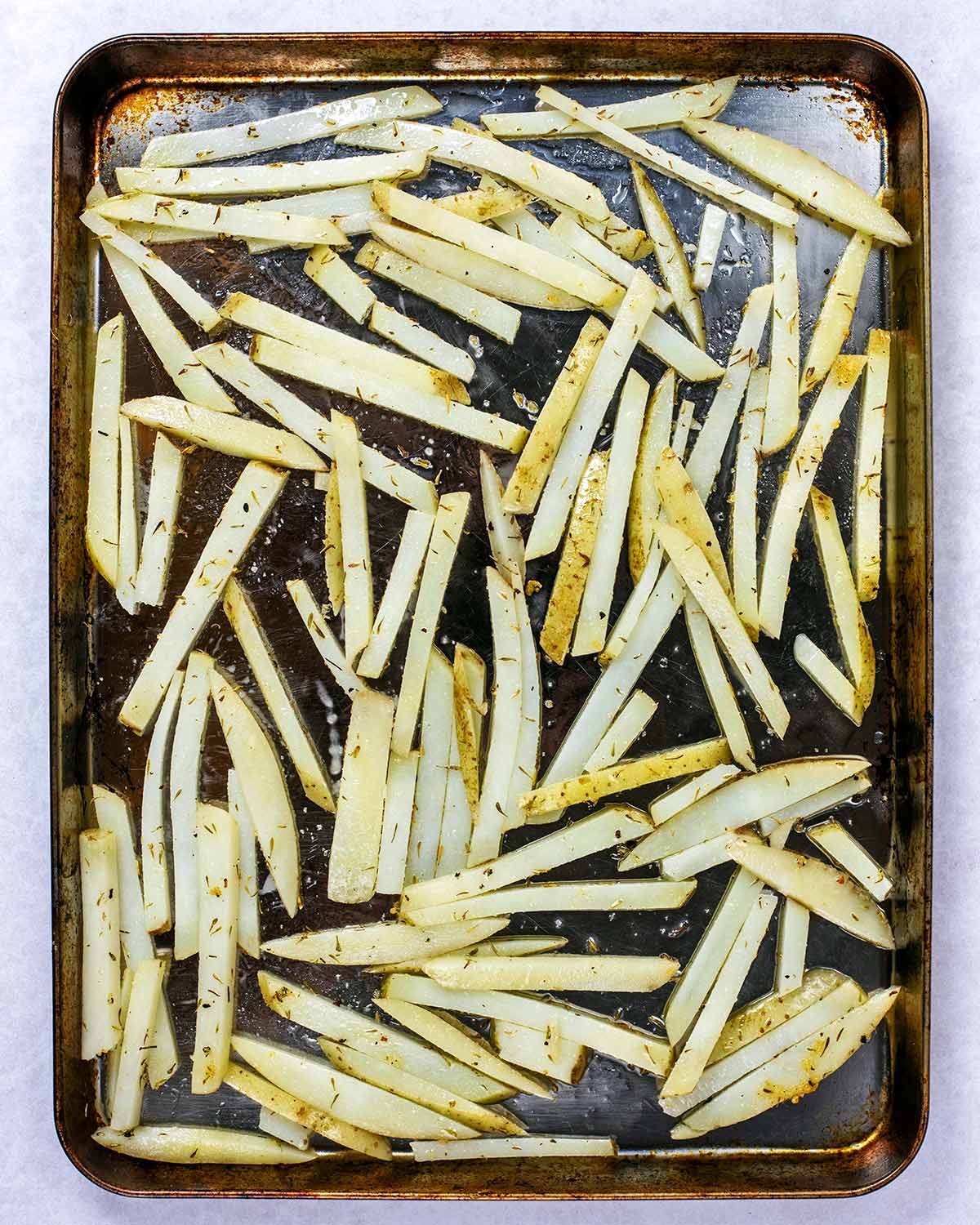 A baking tray covered in parboiled and seasoned fries.