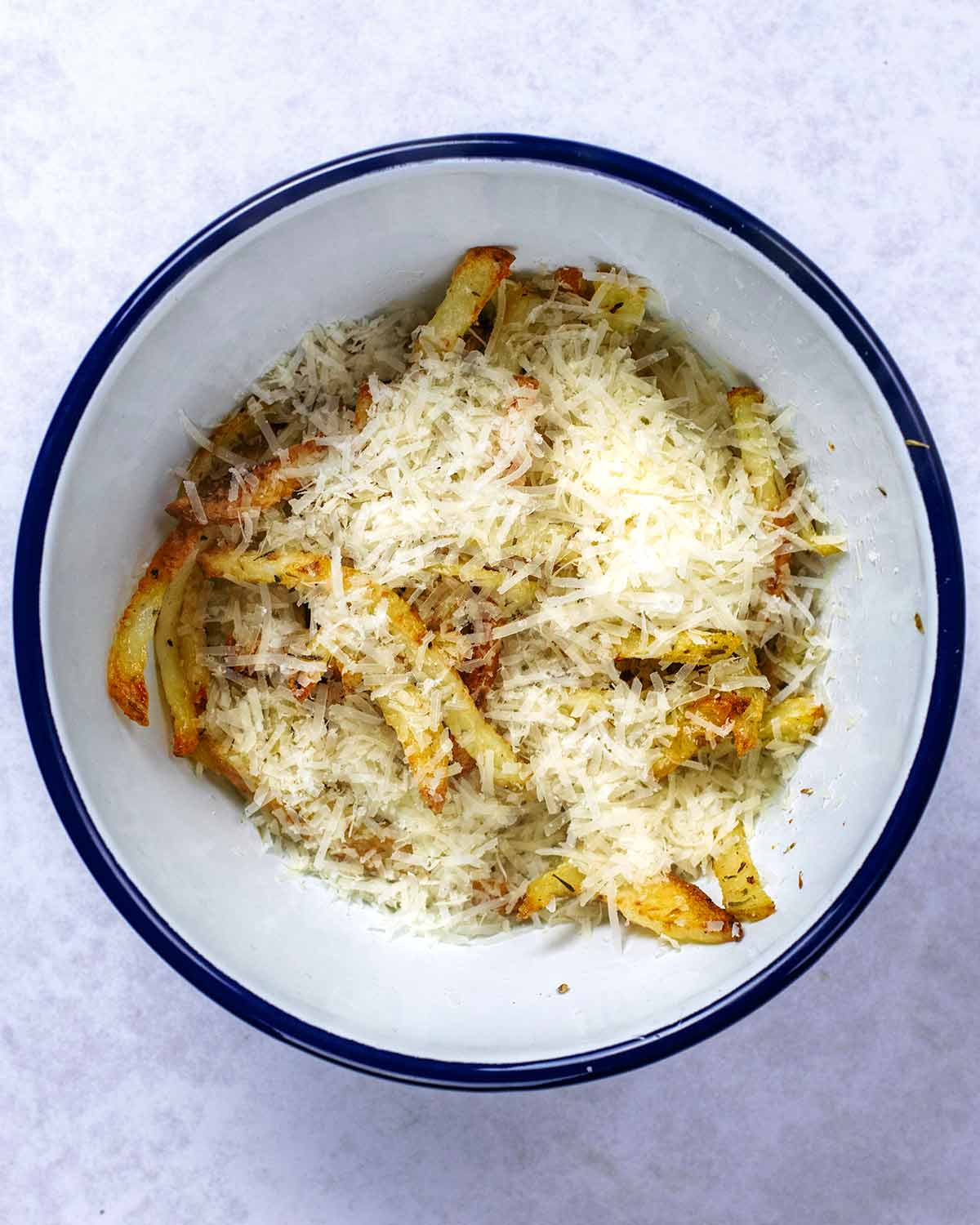 Cooked fries in a bowl covered in grated Parmesan cheese.