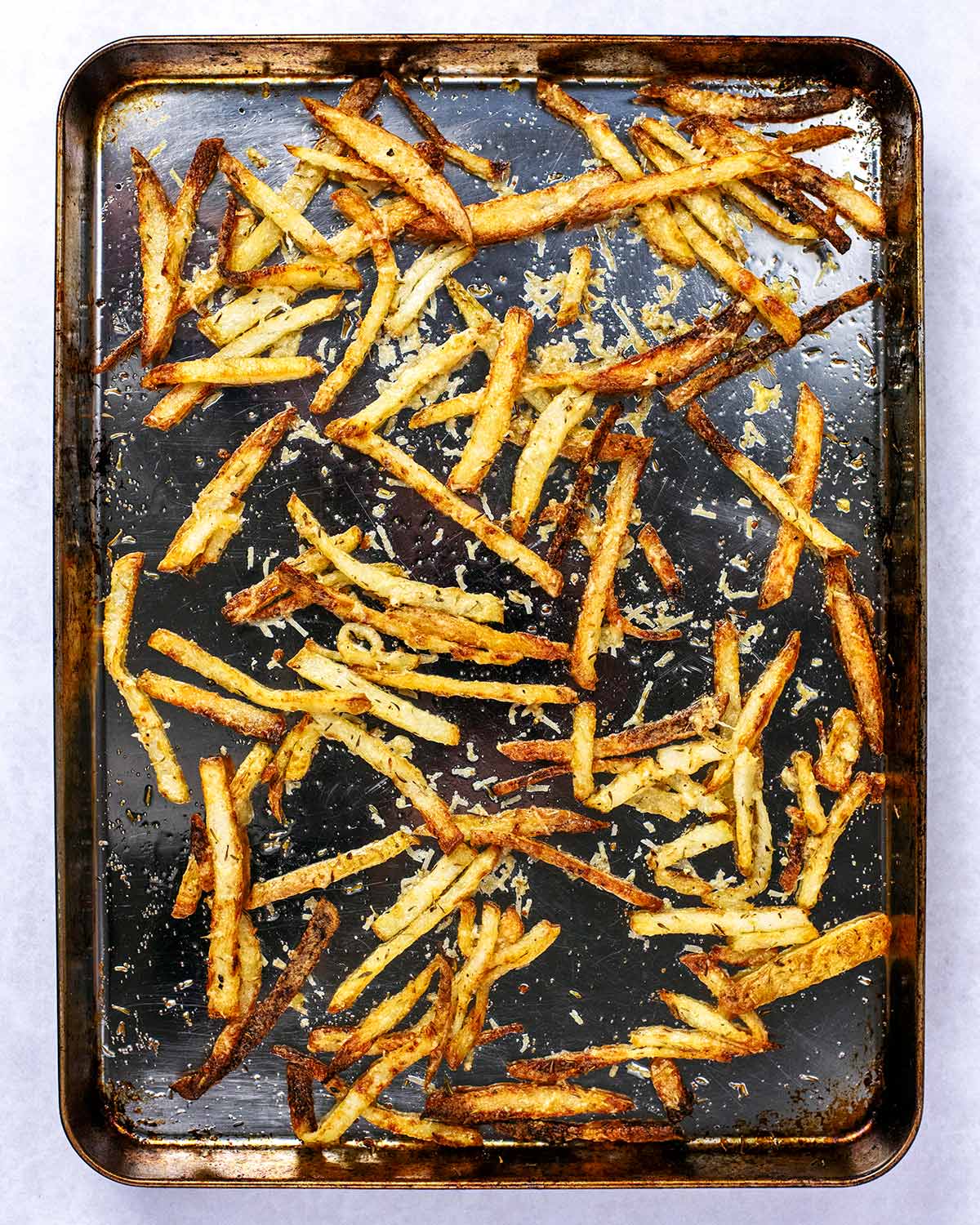 Cooked Parmesan coated fries on a baking tray.