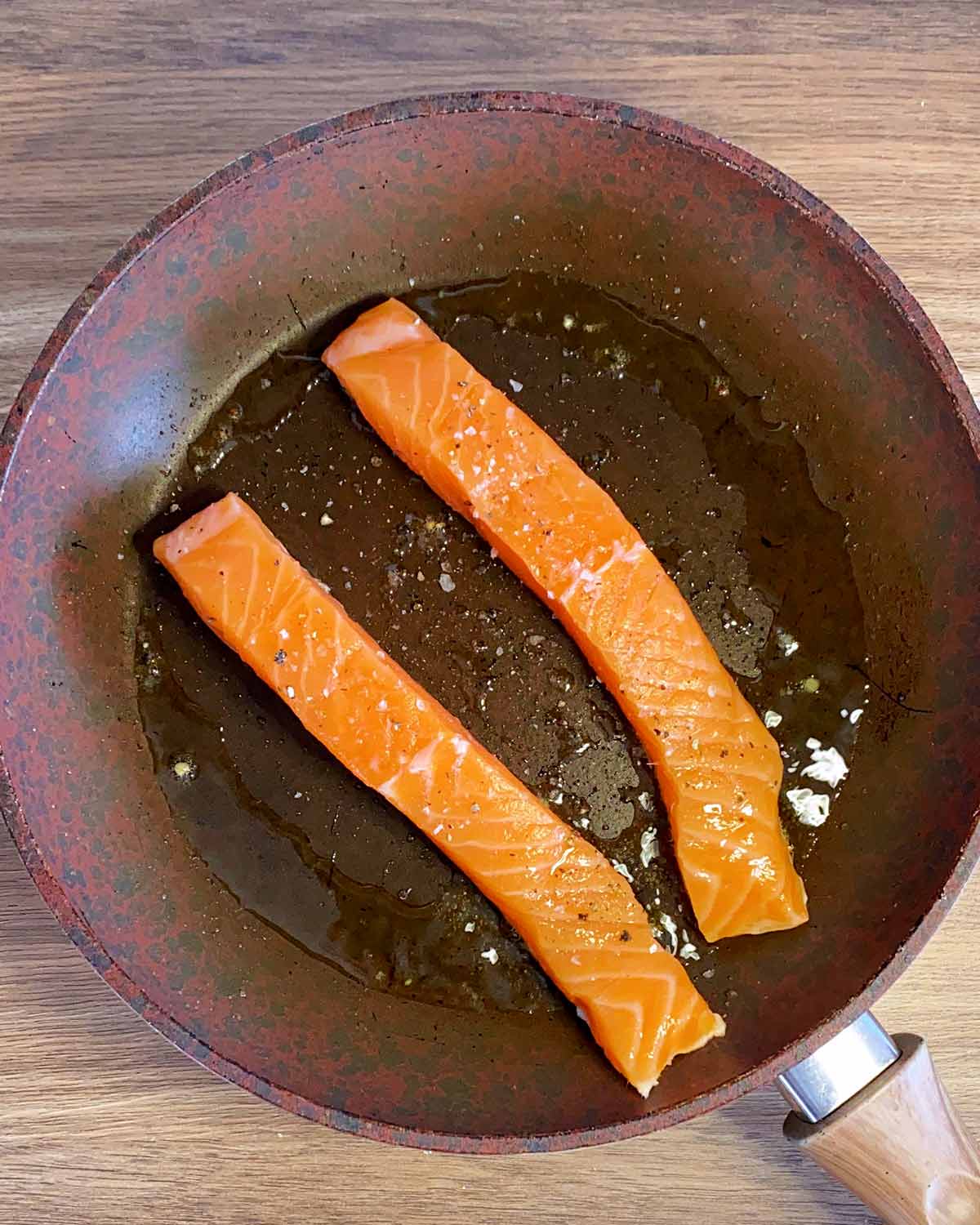 Two salmon fillets cooking in a frying pan.