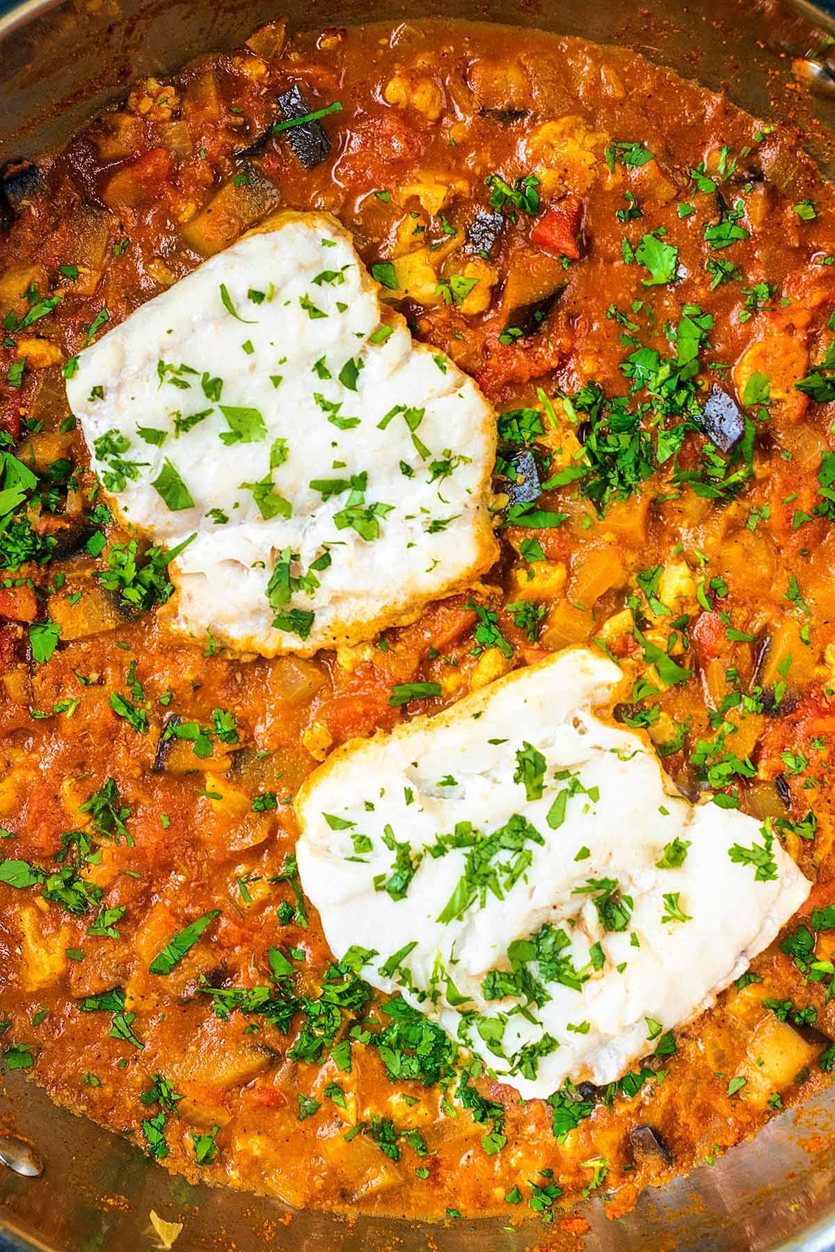 Two cooked cod fillets on top of a curry sauce topped with chopped coriander.