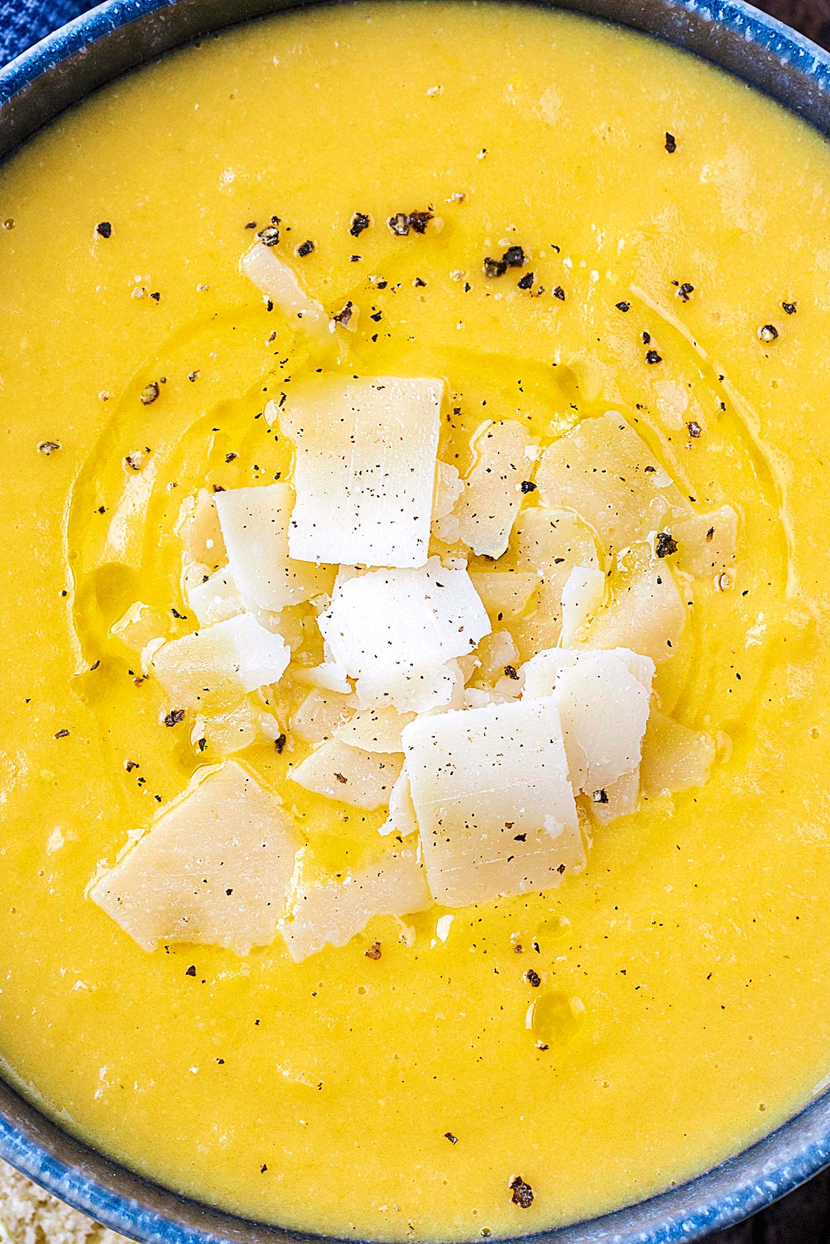 Parmesan shavings and cracked black pepper on the top of a bowl of soup.