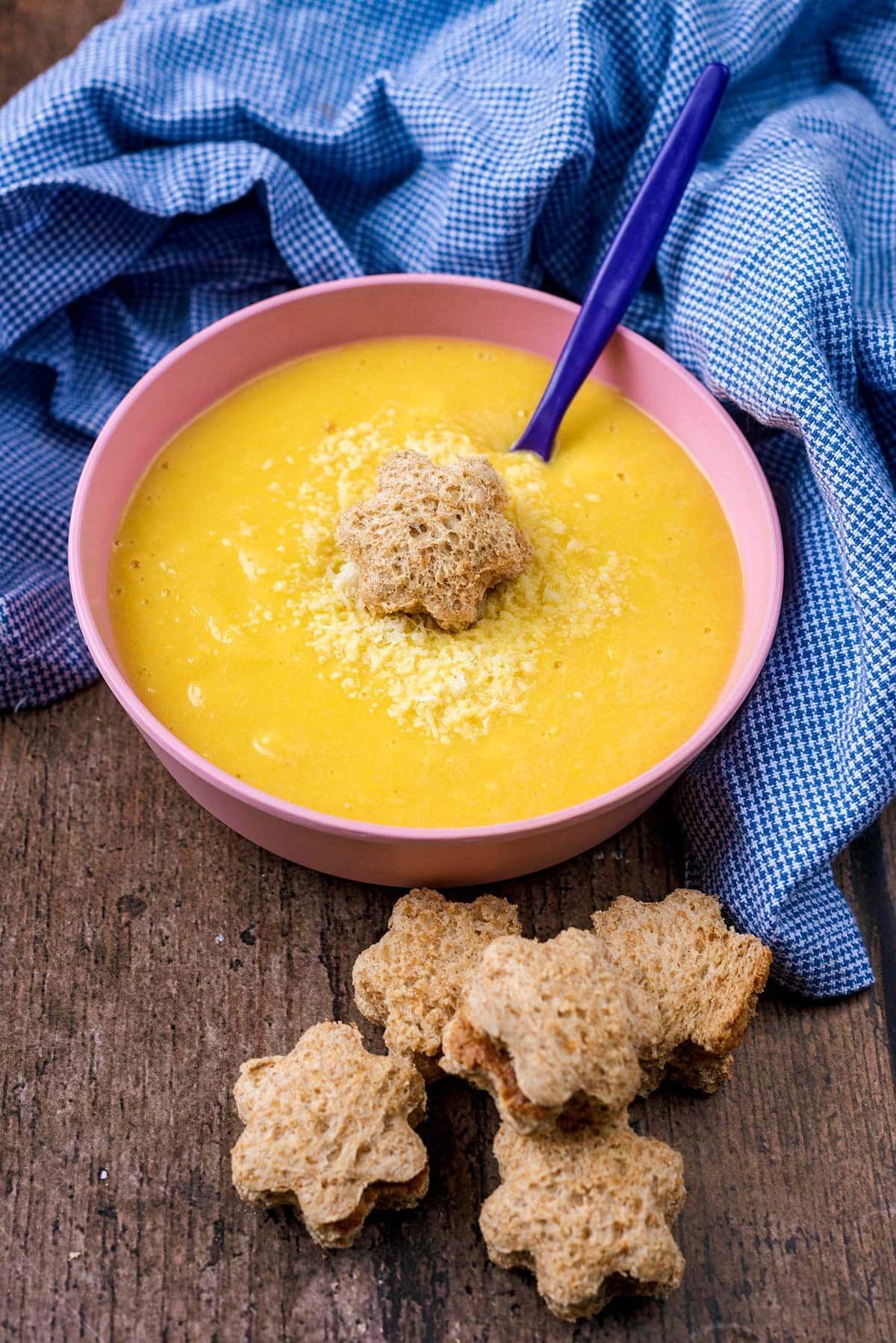 A pink children's bowl with soup and a star shaped piece of bread.