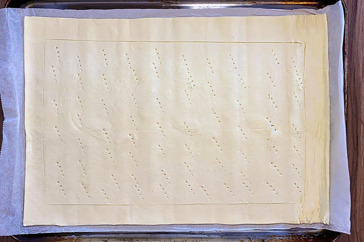 A sheet of uncooked puff pastry with a boarder scored and fork prick marks.