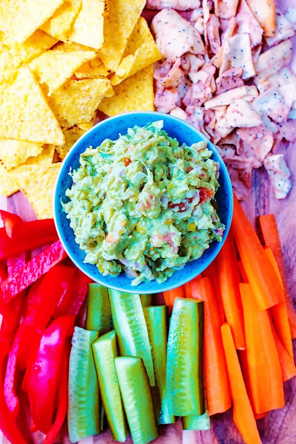a bowl of guacamole surrounded by tortilla chips and crudités.