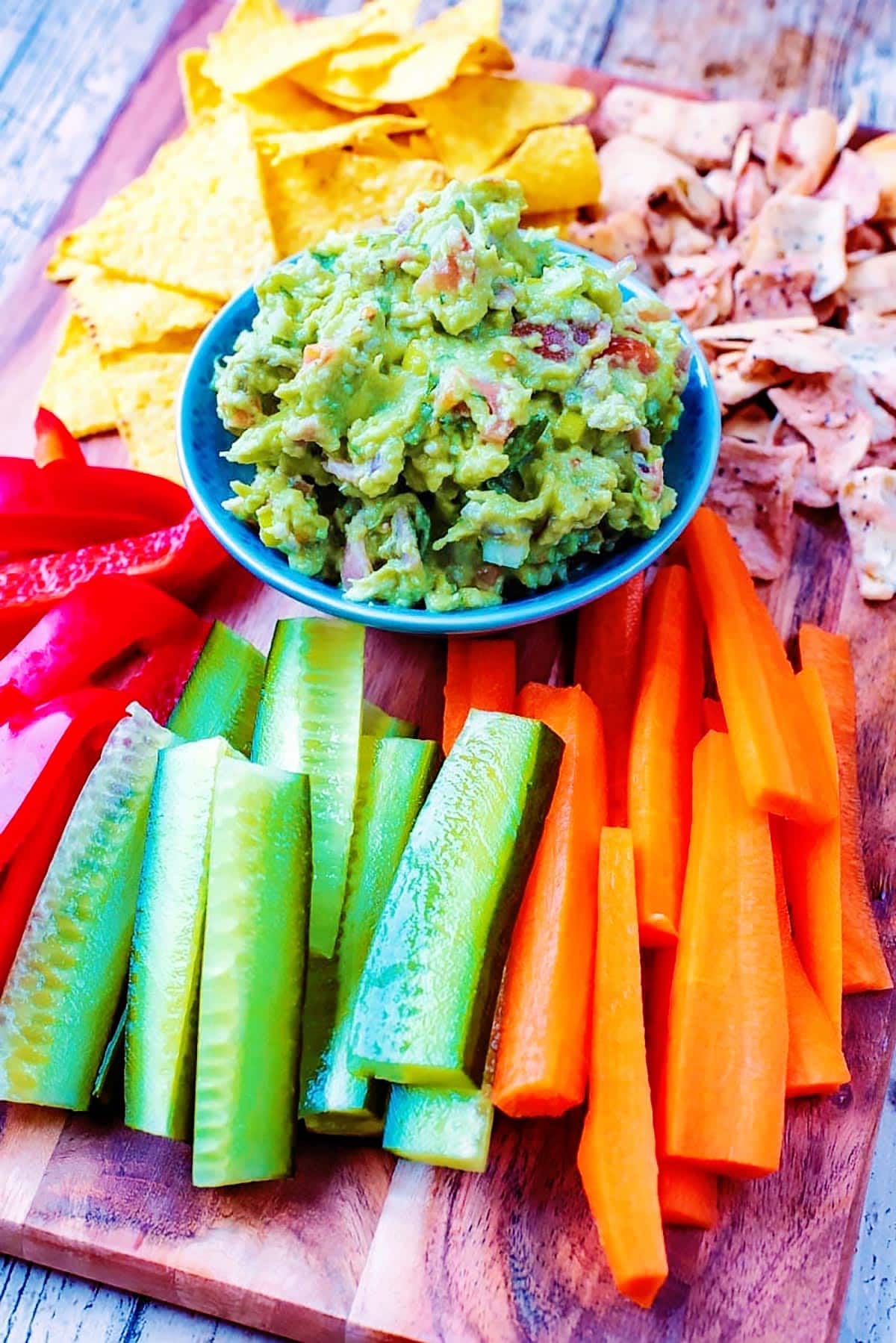 A bowl of guacamole on a serving board with crudités.
