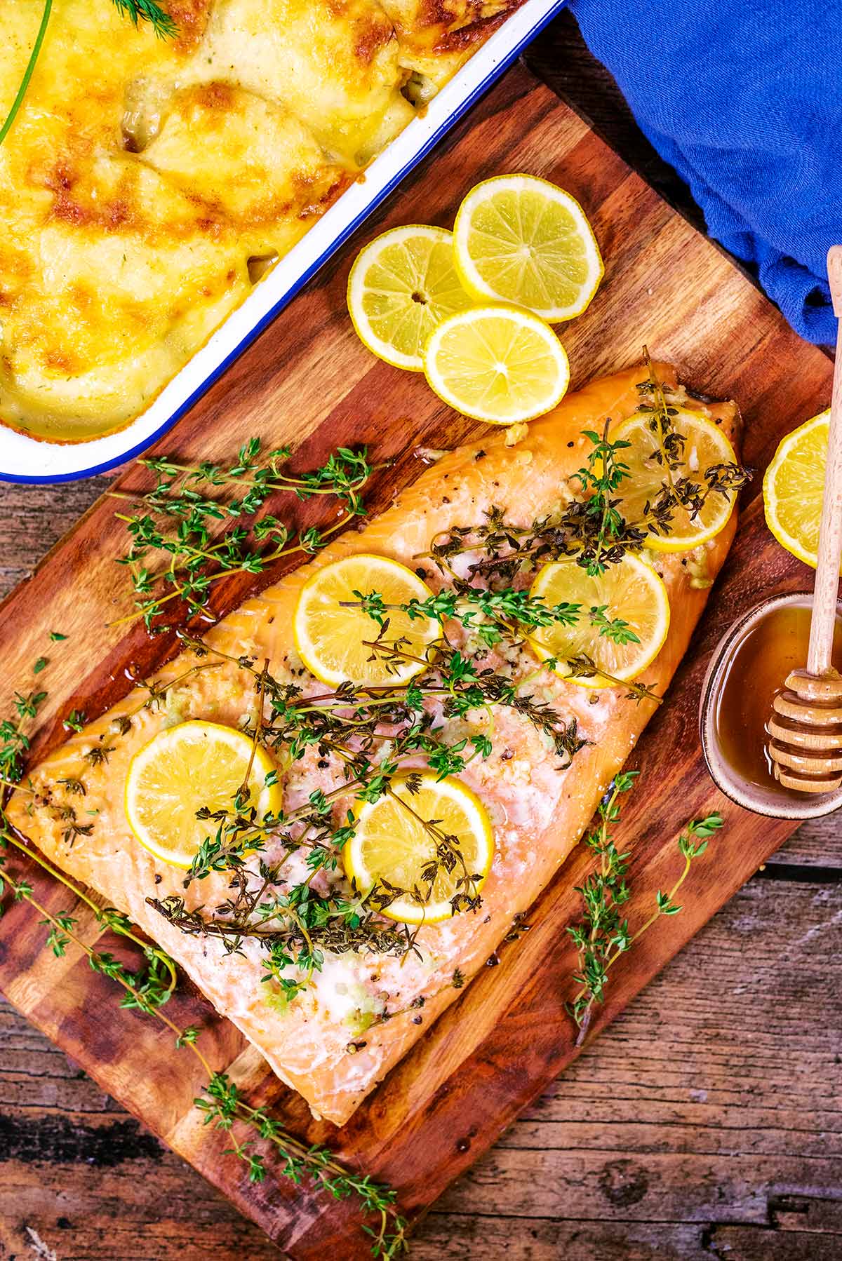 A side of cooked salmon on a wooden board topped with lemon slices and sprigs of thyme.