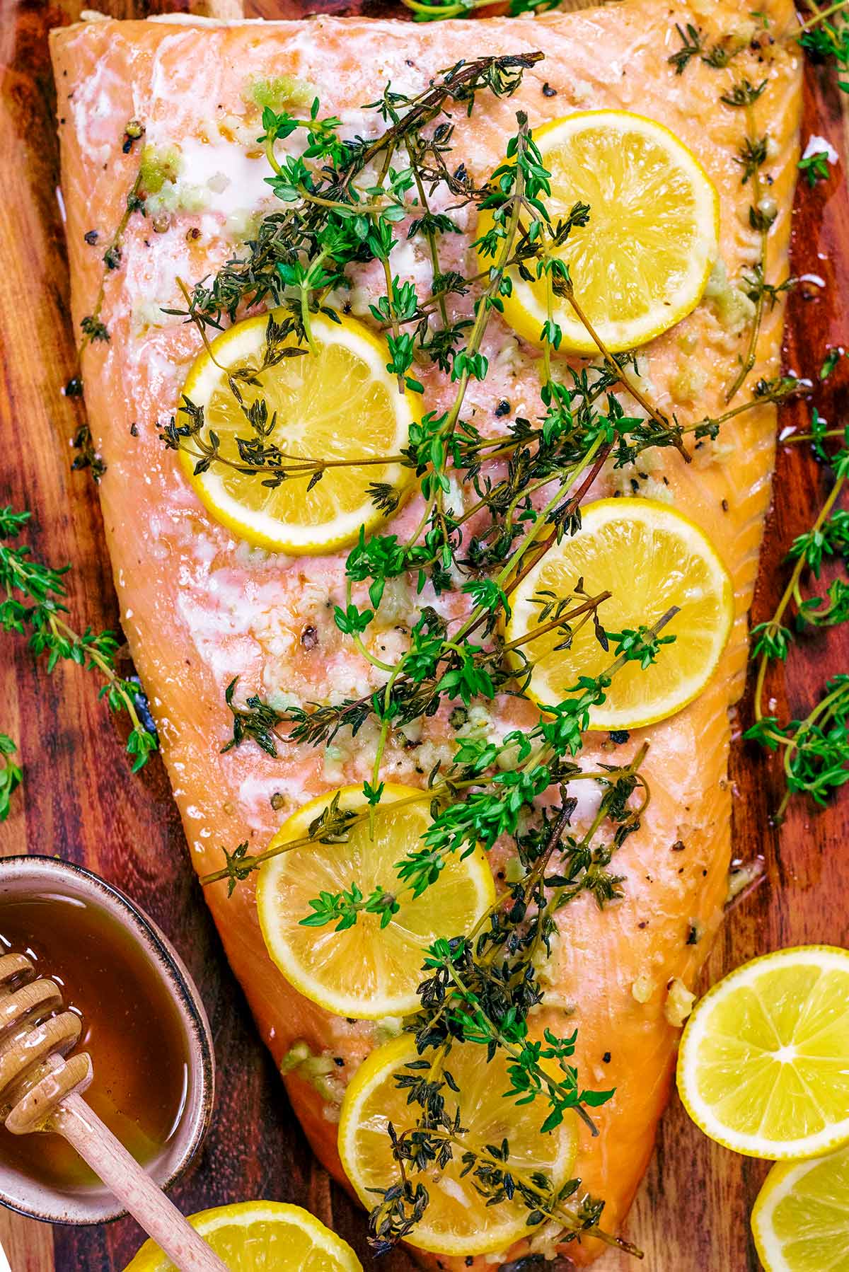 Slices of lemon and sprigs of thyme on top of a cooked side of salmon.
