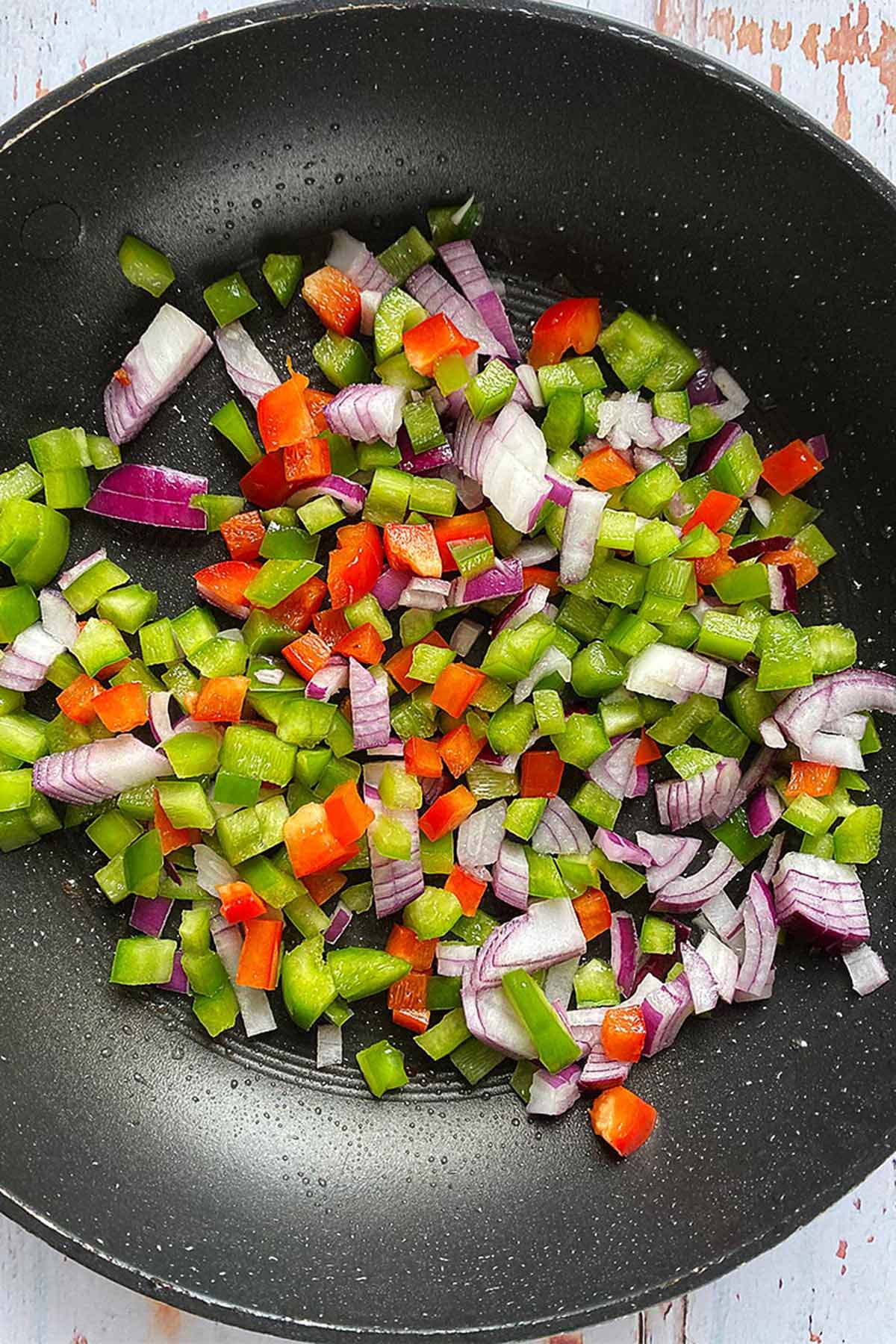 Chopped onion and bell pepper cooking in a frying pan.