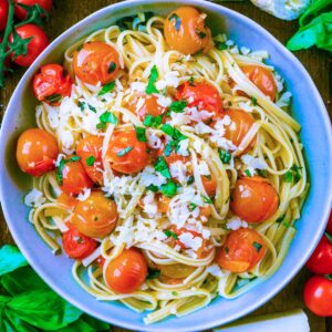 Cherry Tomato Psta in a blue bowl surrounded by tomatoes and basil leaves.