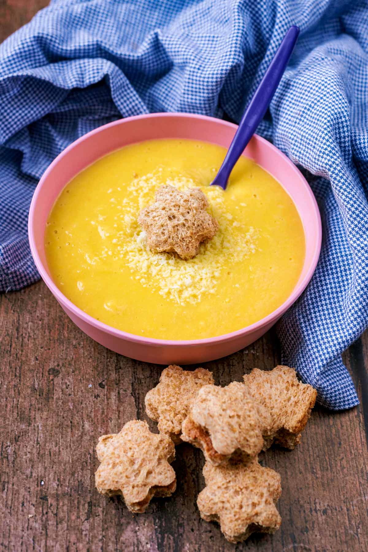 A pink children's bowl with soup and a star shaped piece of bread.