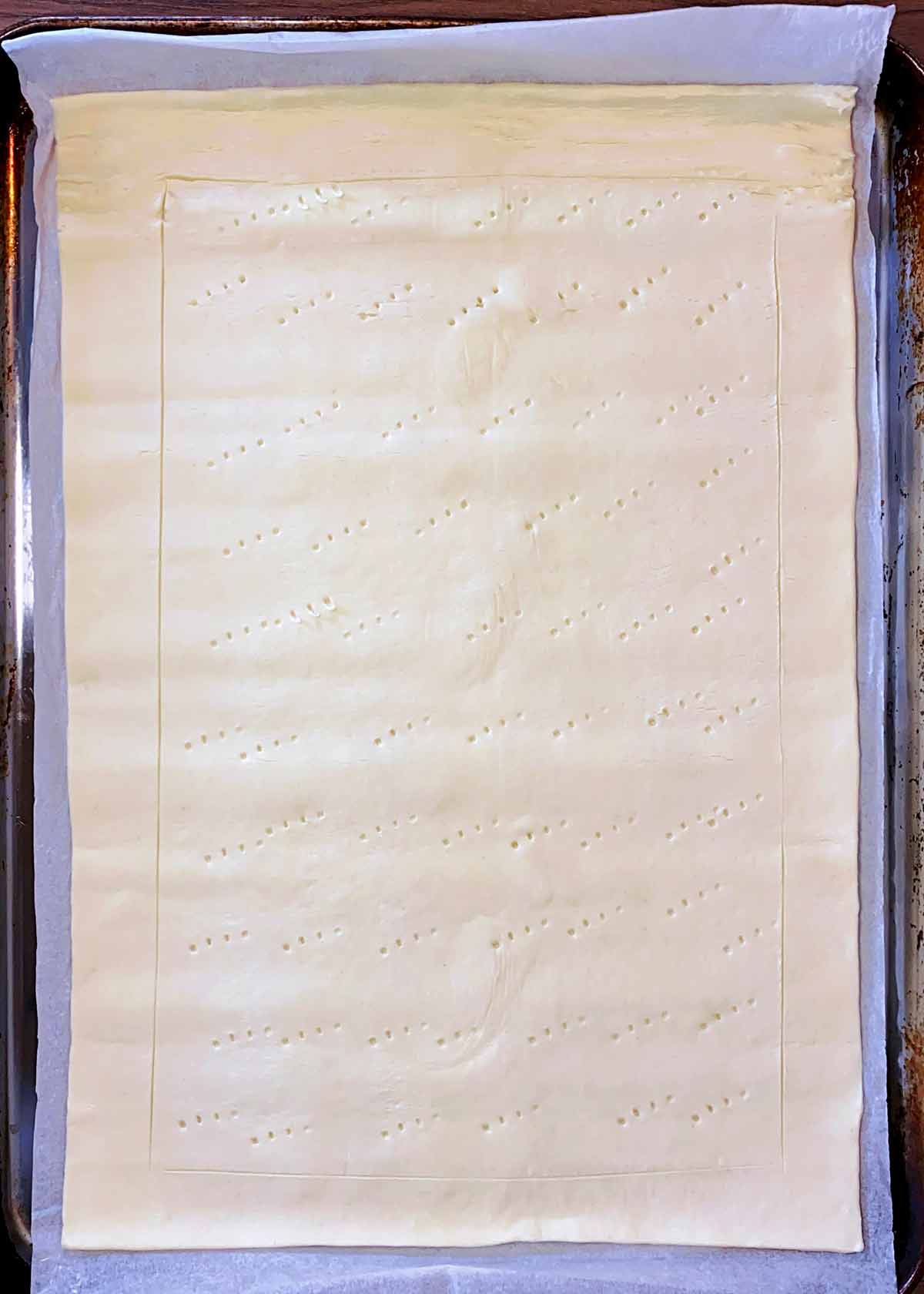 A sheet of uncooked puff pastry with a boarder scored and fork prick marks.