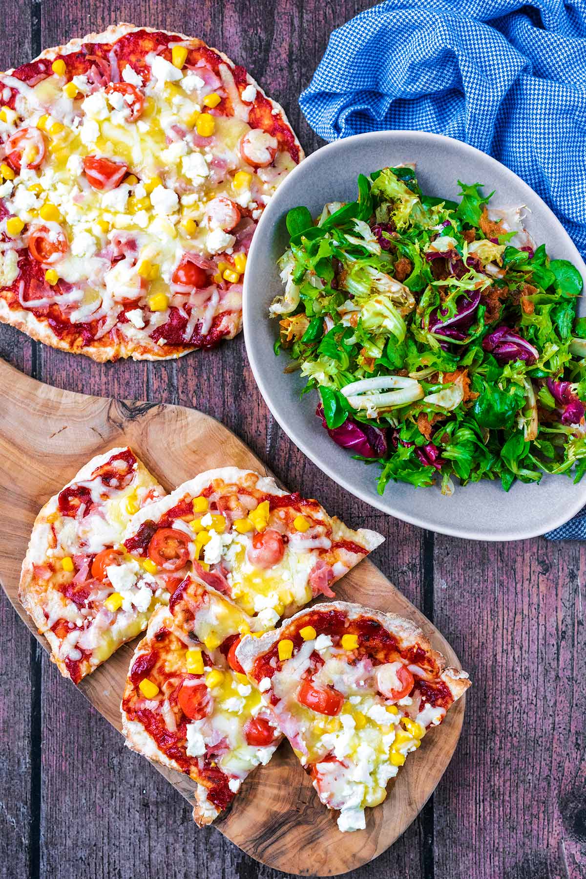Two pizzas, one cut into slices, next to a bowl of salad.
