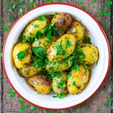 A bowl of Four Herb Roasted Potatoes in a red rimmed white bowl.