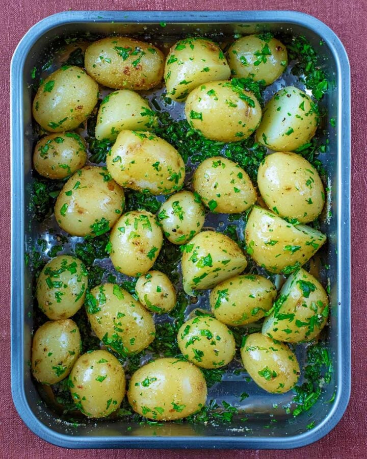 A roasting tin full of halved baby potatoes and herbs.
