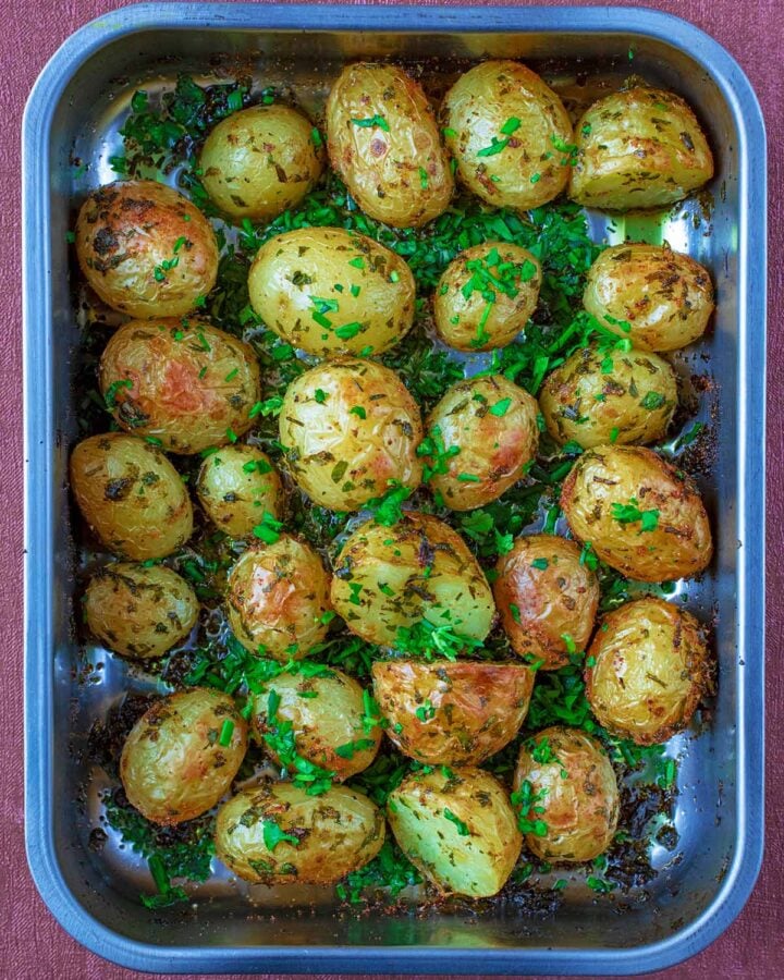 A roasting tin full of roasted halved baby potatoes topped with herbs.