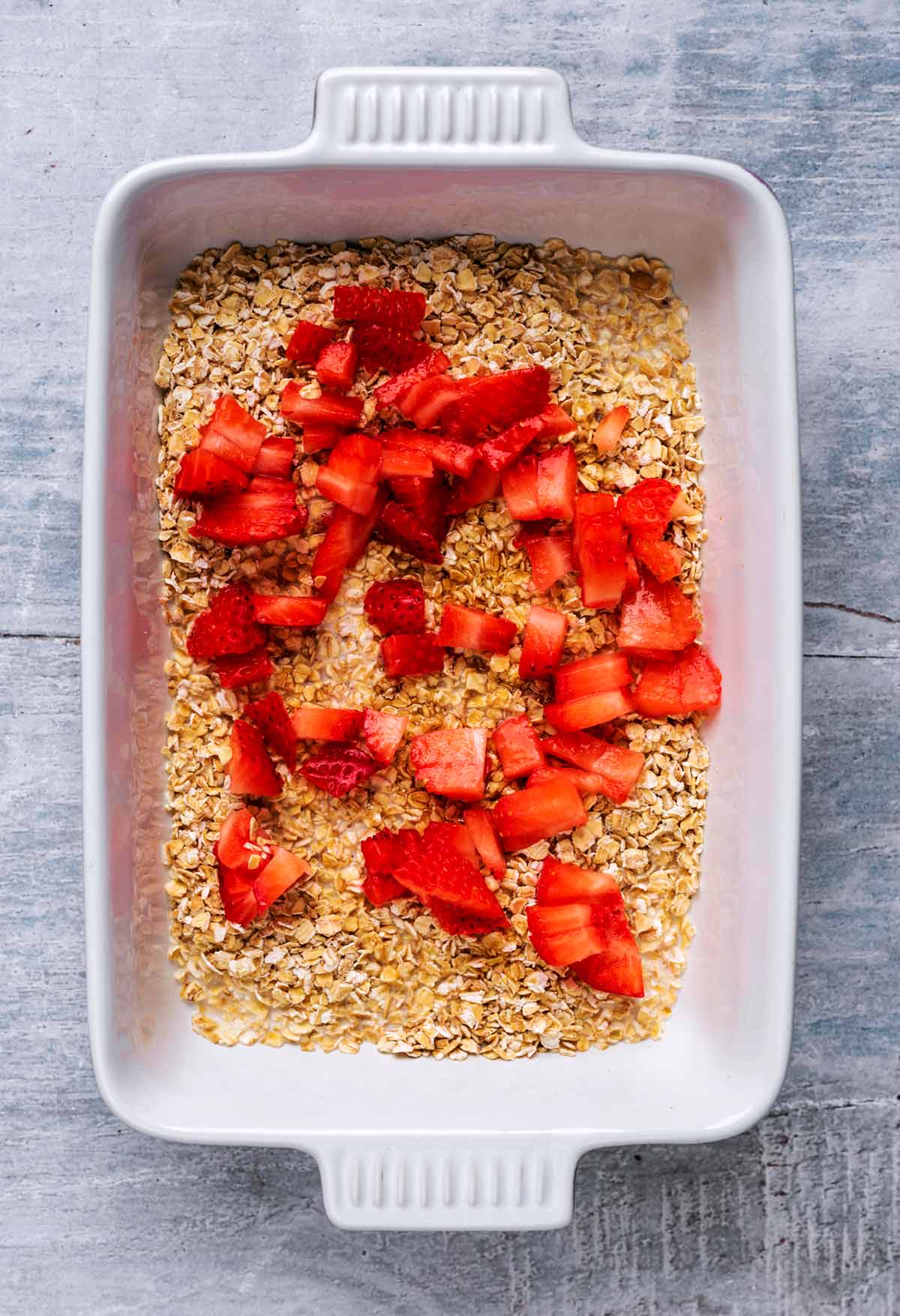 A baking dish containing oats, milk and chopped strawberry.