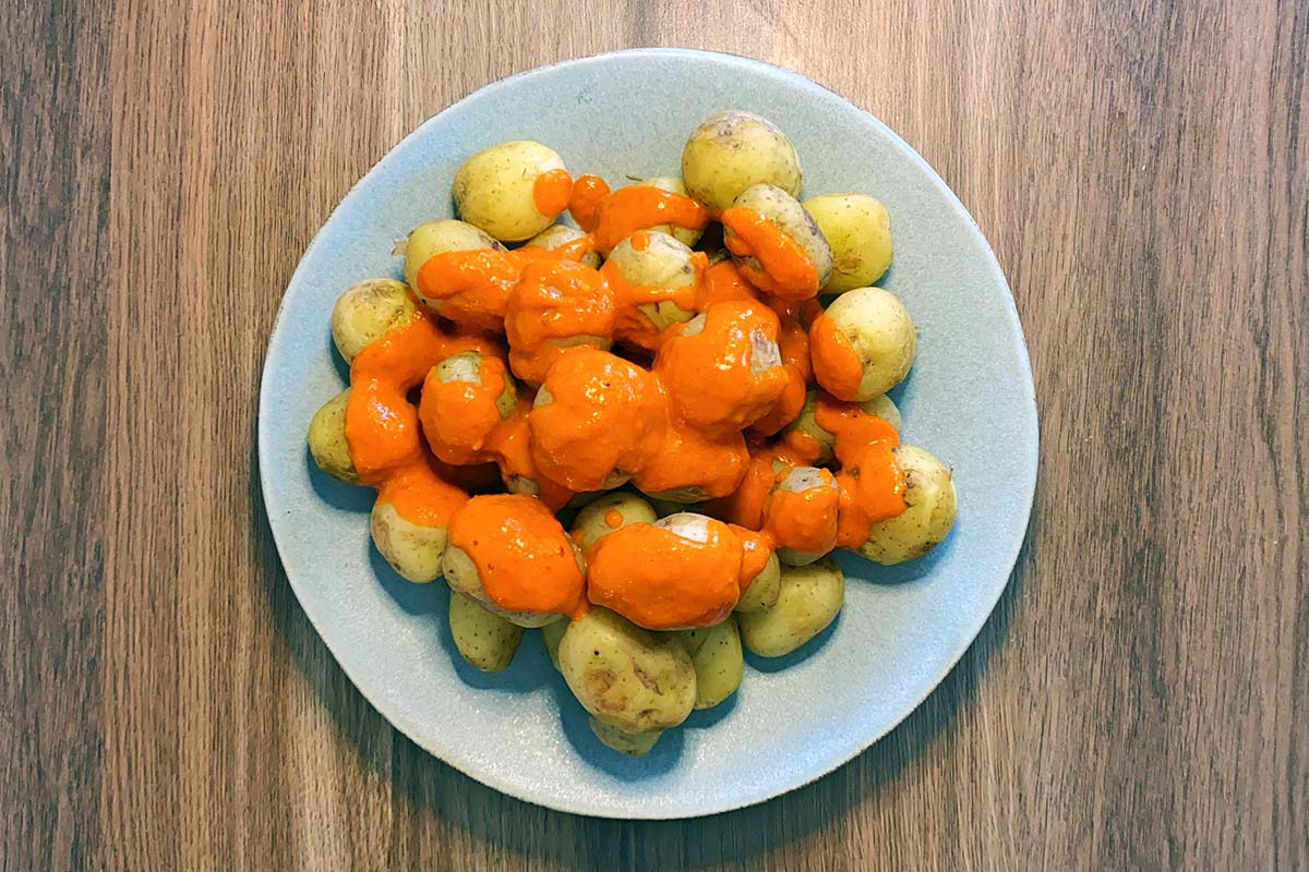 Cooked new potatoes on a plate covered in mojo picon sauce.