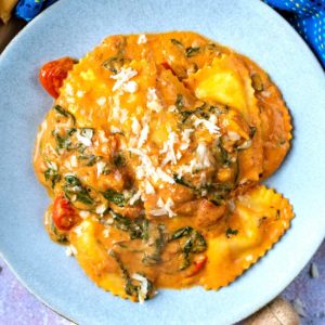 Easy ravioli sauce mixed into ravioli topped with Parmesan shavings.