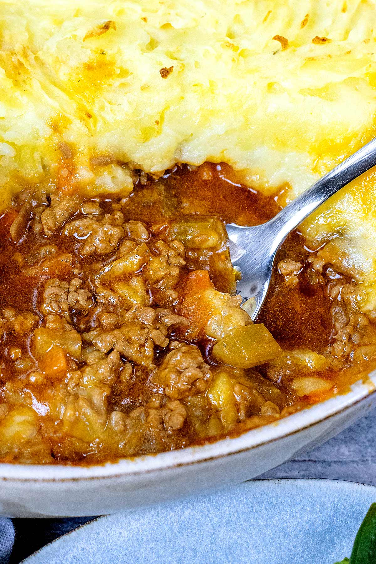 A spoon removing some mince from a large dish of shepherd's pie.