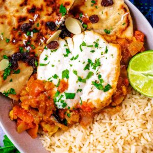 A bowl of cod curry with rice and naan breads.