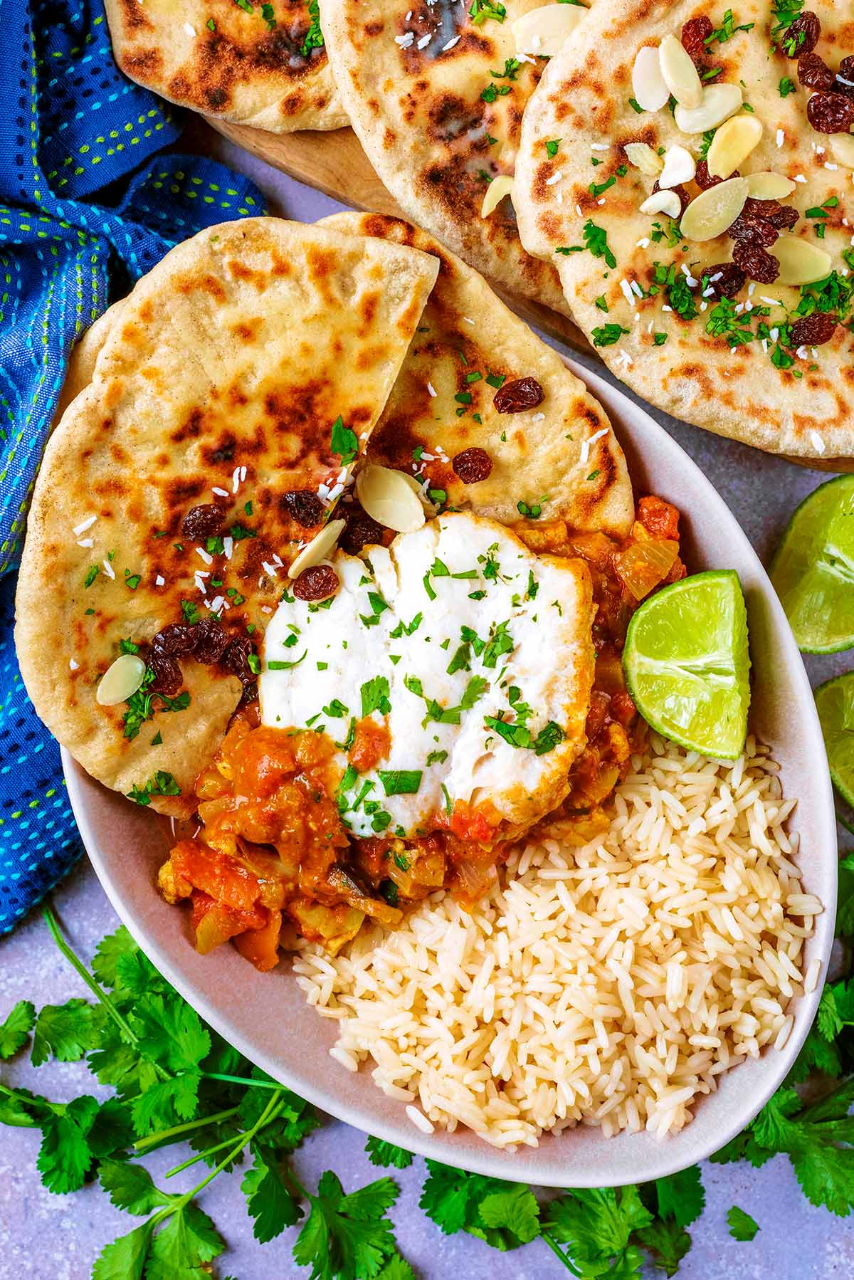 A bowl of cod curry, rice and naan bread next to a blue towel.