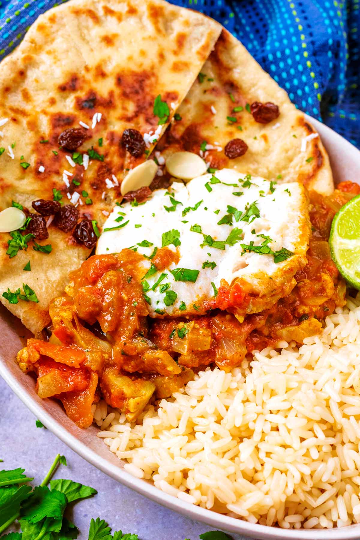 Cooked cod on top of curry sauce with naan breads and rice.