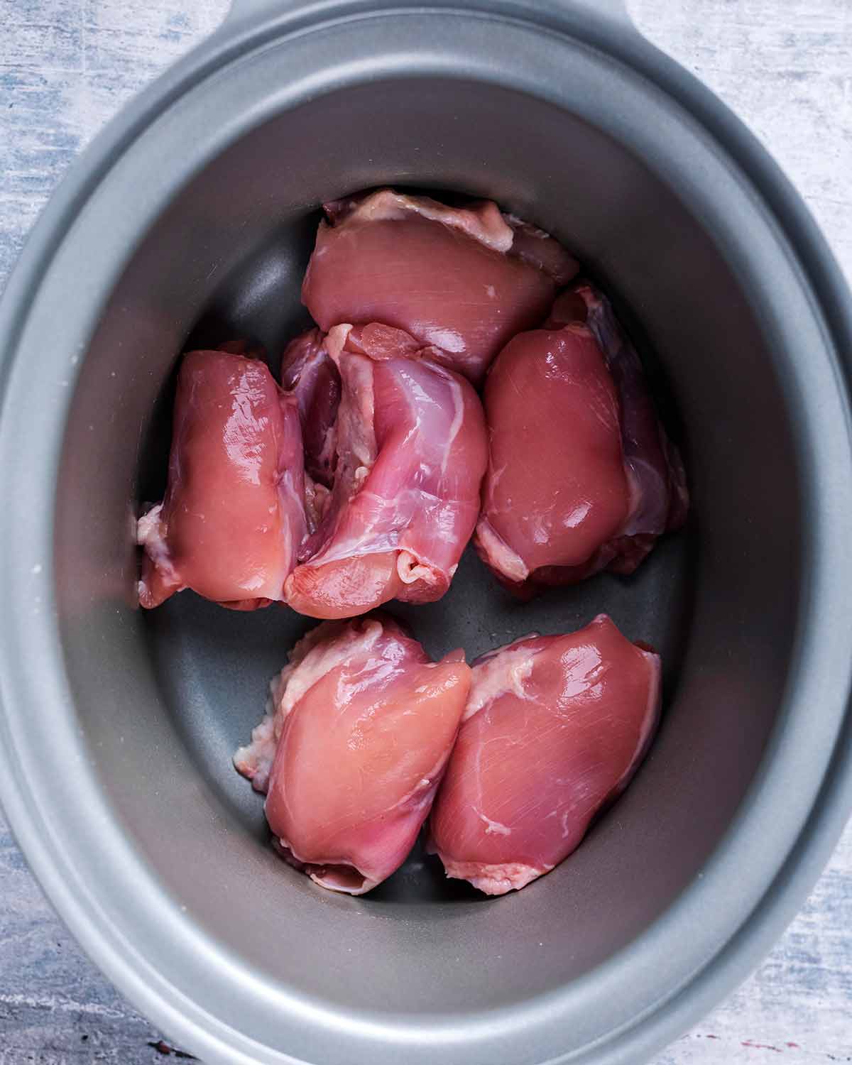 A slow cooker pot with six chicken thighs in it.