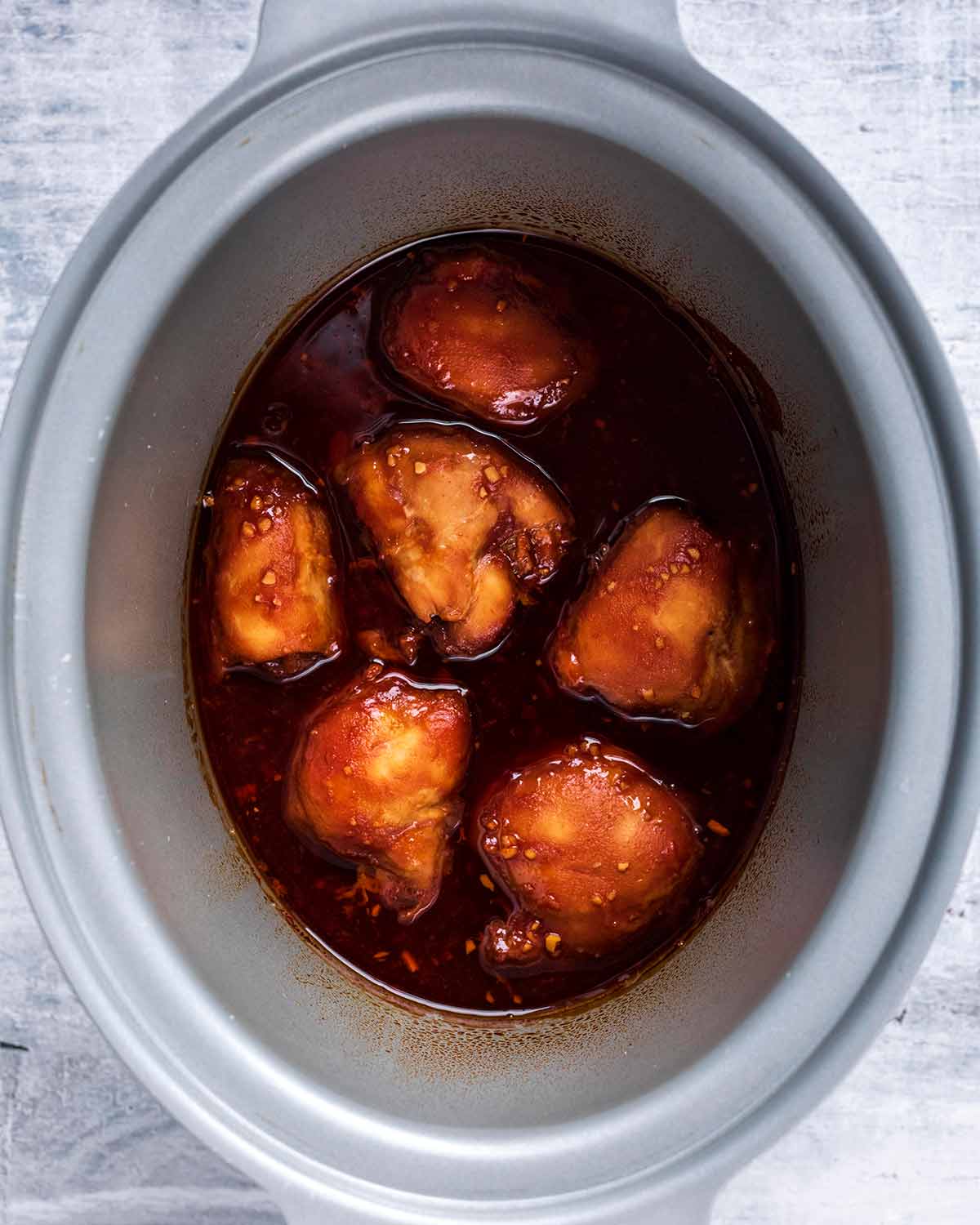 Cooked chicken thighs in a soy tomato sauce in a slow cooker bowl.