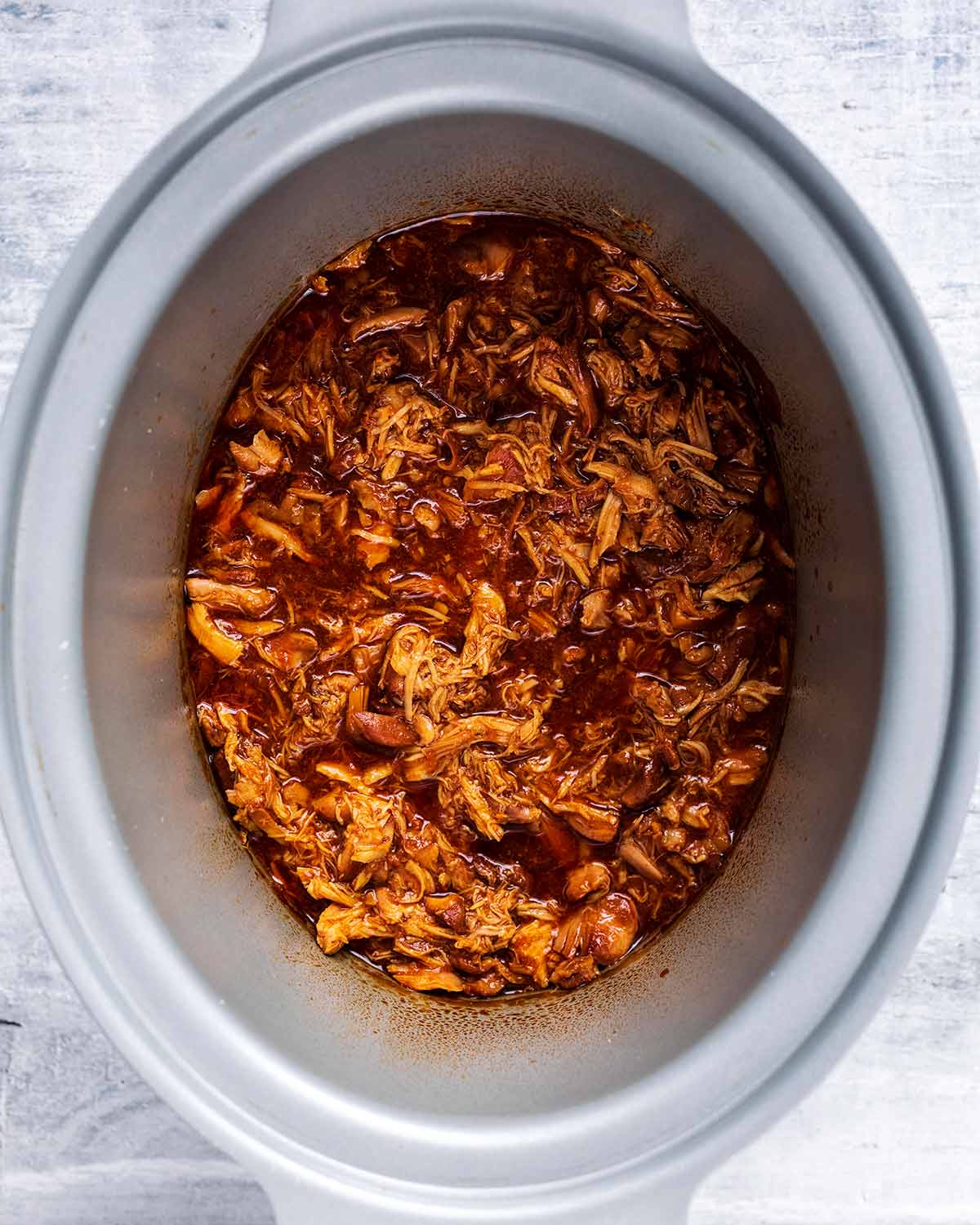 The chicken has been shredded and mixed with the sauce in the slow cooker bowl.