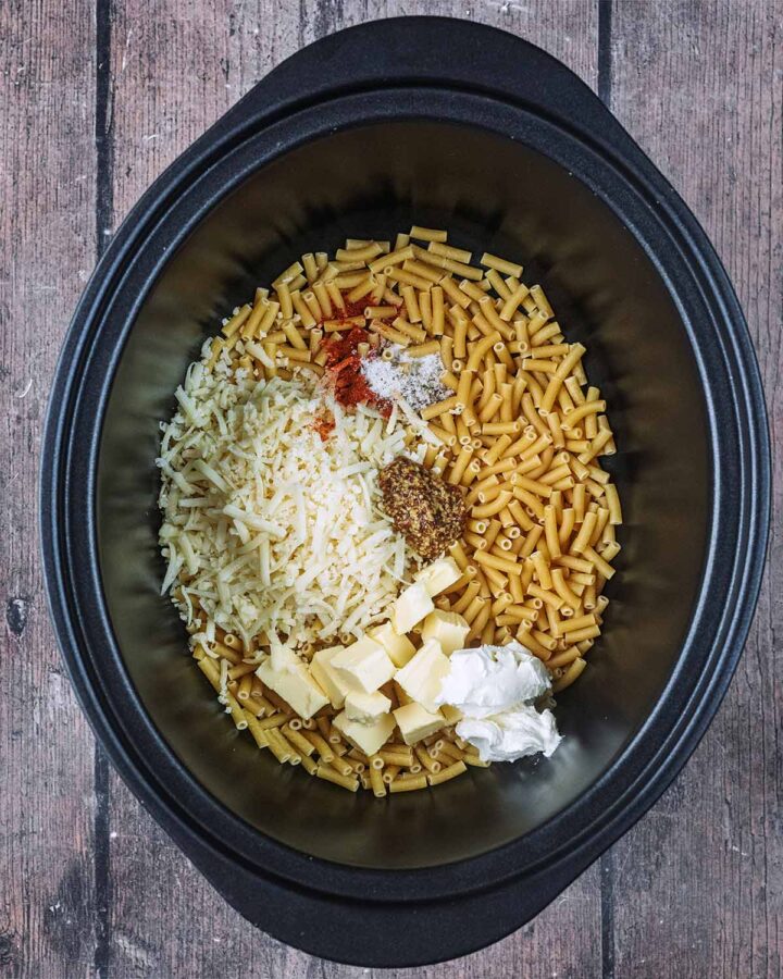 Dry macaroni, grated cheese, butter, mustard and seasoning in a slow cooker bowl.